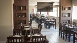 Un restaurante espacioso con varias mesas y sillas, paneles de madera y un televisor de pantalla plana grande montado en la pared.