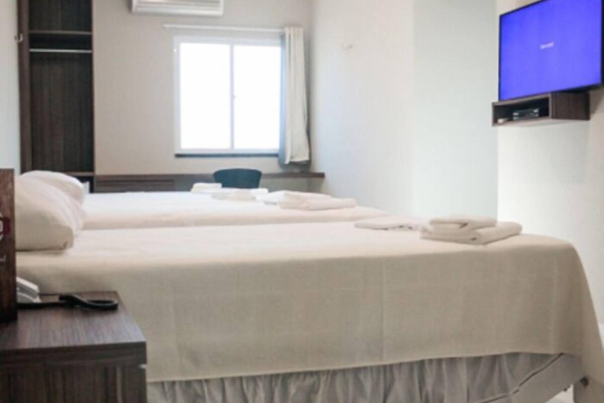 Habitación de hotel con una cama grande, un aparador de madera, un televisor de pantalla plana en la pared y un equipo de aire acondicionado.