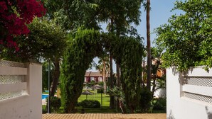 Un cancello chiuso con un vialetto che conduce a un edificio, immerso nel verde e sotto un cielo sereno.