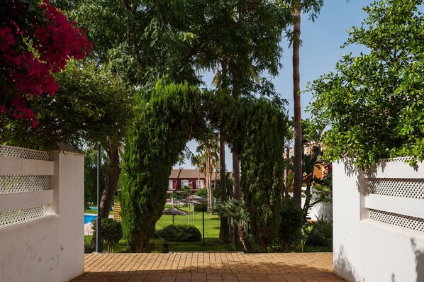 A gated entrance with a pathway leading to a building, surrounded by lush greenery and a clear sky.