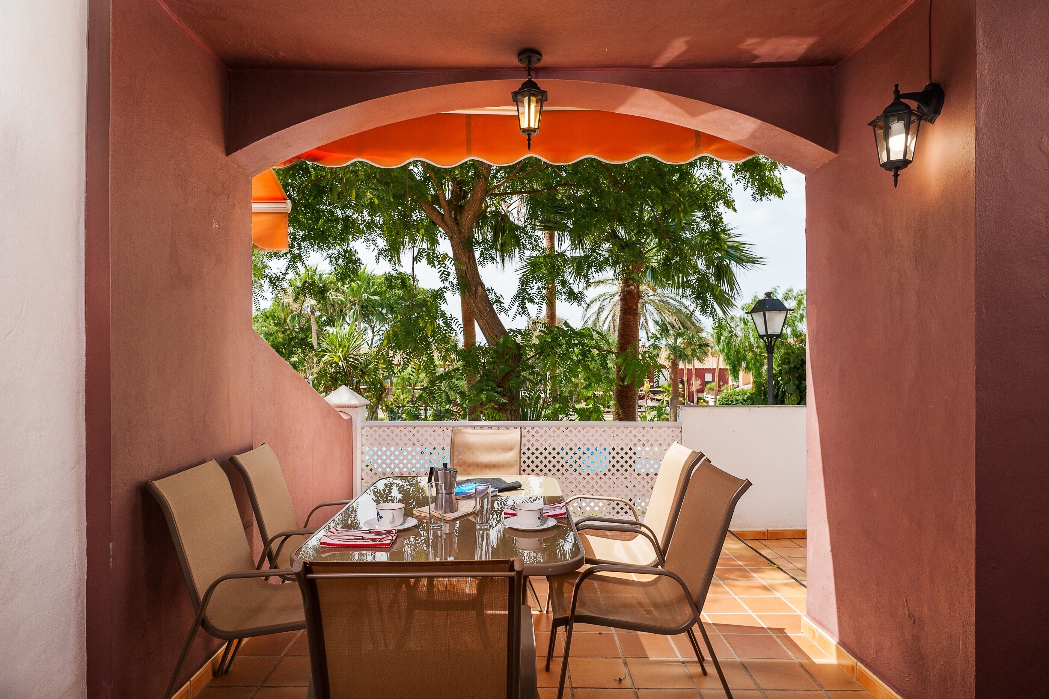 Une terrasse extérieure avec une table et des chaises, un plafond décoratif et une vue sur les arbres et les bâtiments.