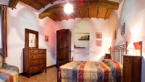 Un dormitorio con techo de madera, una cama con colcha estampada, un aparador y una mesita de noche con lámpara.