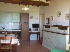 Una cocina con armarios de madera, una mesa de comedor, sillas, un microondas y un televisor.