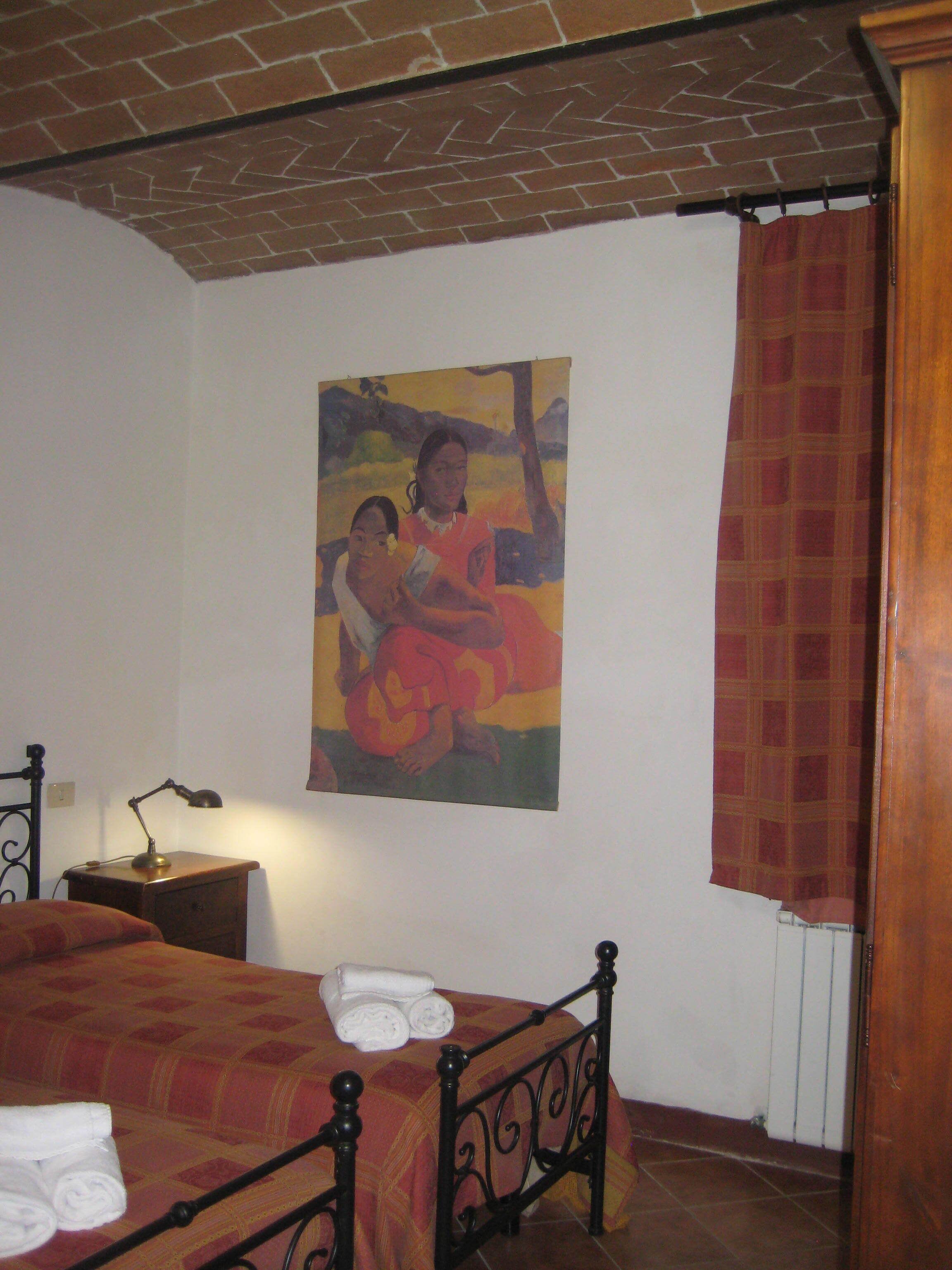 Une chambre à coucher avec un lit, une table de chevet, une lampe, un tableau et une fenêtre avec un rideau.