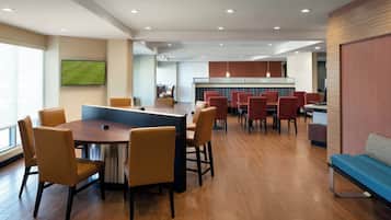 A modern hotel lobby with a central dining area, a bar, and a seating area with a blue couch.
