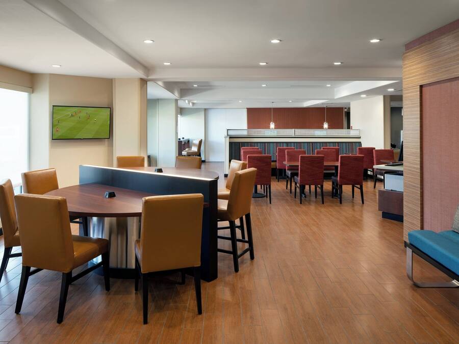 A modern hotel lobby with a central dining area, a bar, and a seating area with a blue couch.