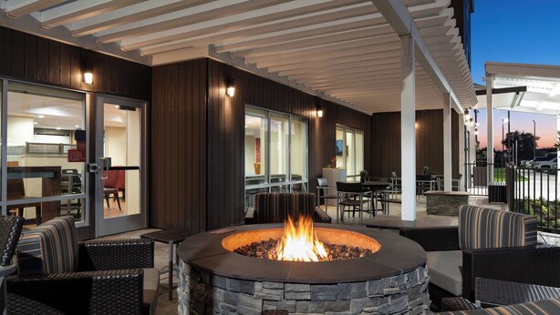 Une terrasse extérieure dotée d’un foyer en pierre, entourée de meubles en osier, d’un espace salon couvert et offrant une vue sur la salle à manger intérieure.