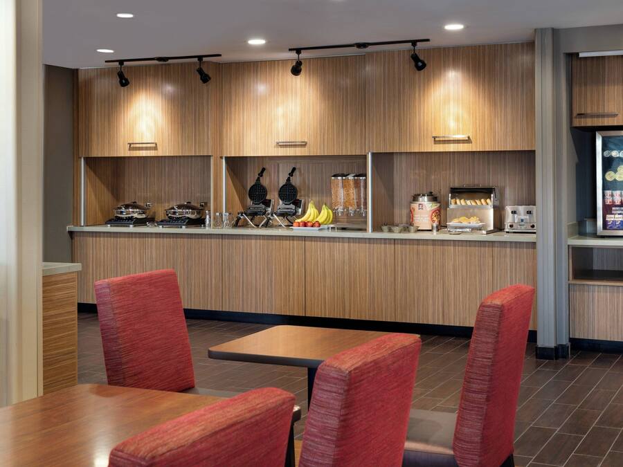 A modern restaurant with wooden paneling, a self-service counter, and red upholstered chairs.