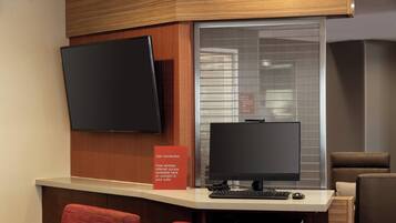 A hotel reception desk with two monitors, a flat-screen TV, and a sign offering free wireless internet.