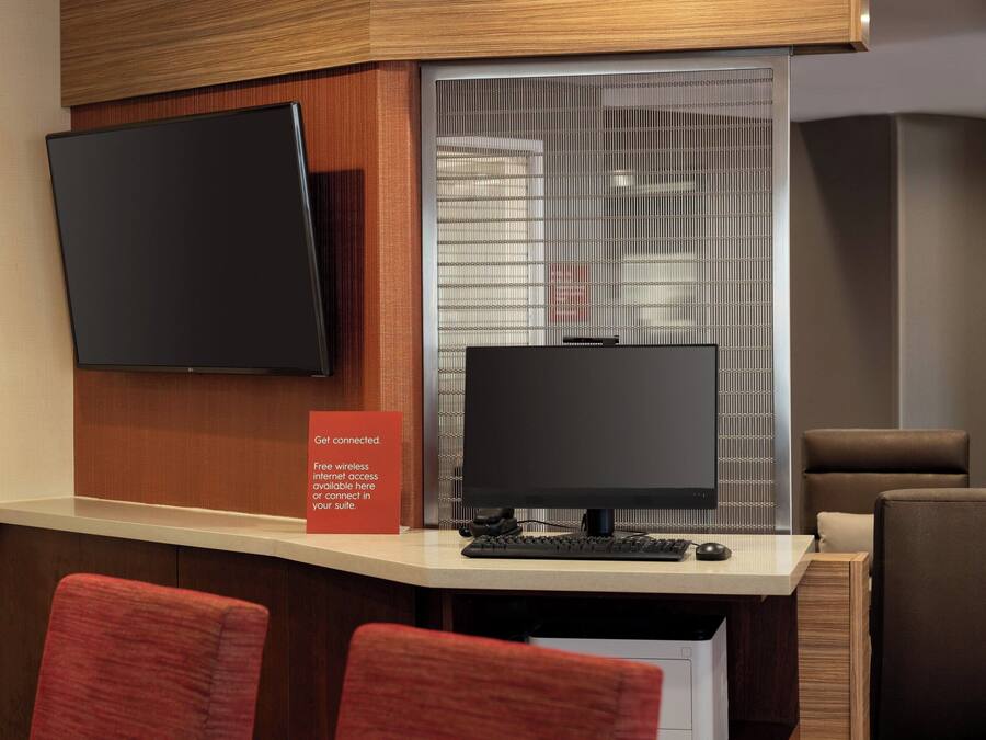 Mostrador de recepción de hotel con dos monitores, un televisor de pantalla plana y un cartel que anuncia internet inalámbrico gratuito.