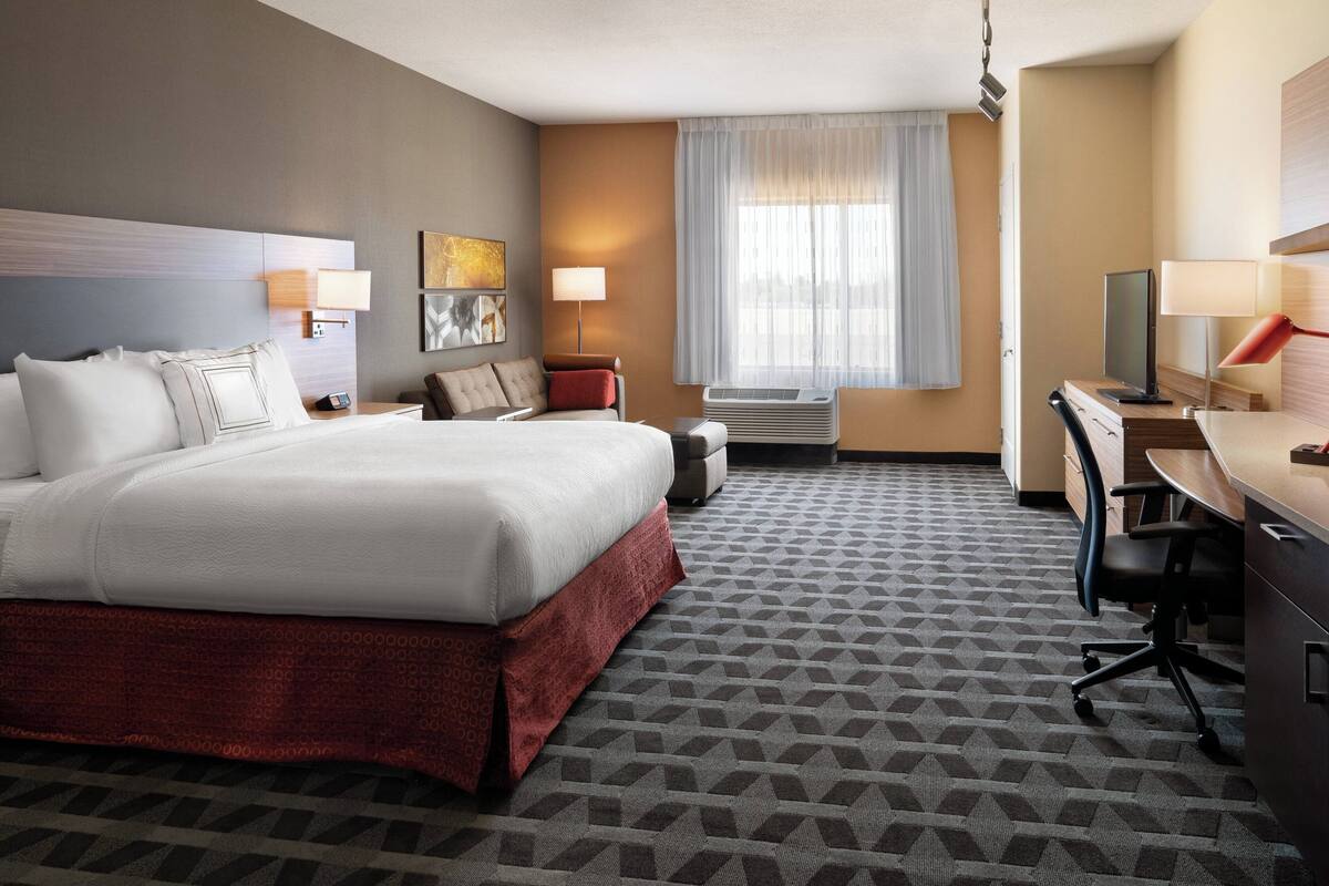 Une chambre d’hôtel avec un grand lit, un bureau, une chaise, une lampe et une fenêtre avec des rideaux.