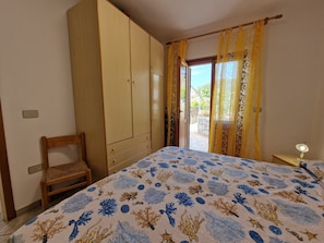 Une chambre à coucher avec un lit, une armoire, une chaise et une vue sur l’extérieur, visible à travers une porte.