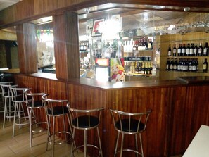 A bar area with wooden bar counter, metal stools, and shelves stocked with bottles. - Complexe Hôtelier Asthoria palace (Abidjan)