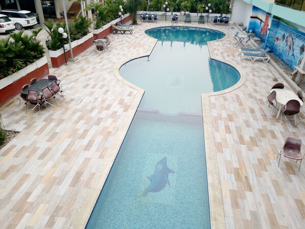 Una piscina con un mural de delfines, rodeada de sillones y mesas.