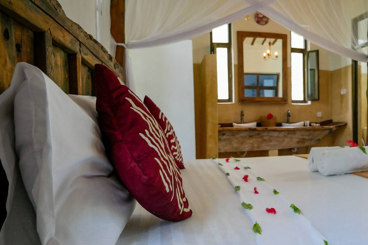 A bedroom with a bed, a wooden bench, a vanity with a mirror, and a window with curtains.