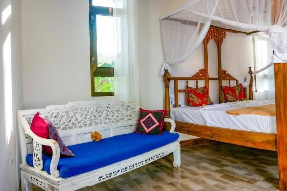 A room with a wooden four-poster bed, a white sofa with blue cushions, and a white chair.