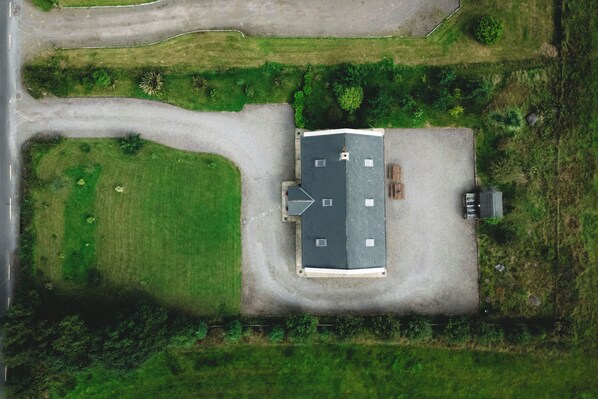 An aerial view of a building with a flat roof, surrounded by green fields and a paved road. - Beautiful Mountain View Home near Killarney National Park (Killarney)