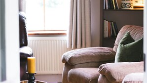 Un accogliente soggiorno con una poltrona in pelle, un tavolino con una candela, una libreria piena di libri e una finestra con tende.