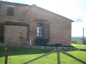 Un bâtiment en briques doté d’une fenêtre, d’une porte et d’un petit espace extérieur aménagé pour s’asseoir.