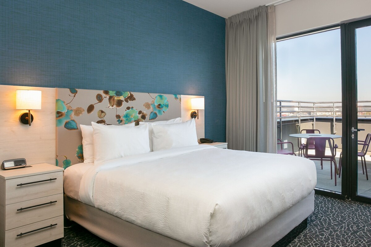 A hotel room with a large bed, two bedside lamps, a nightstand, and a view of the outside balcony.