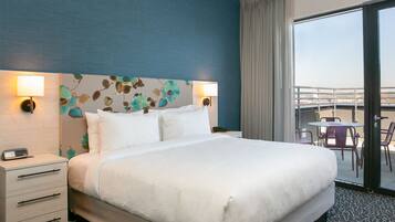 A hotel room with a large bed, two bedside lamps, a nightstand, and a view of the outside balcony.