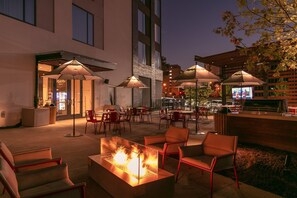 Et udendørs loungeområde med bålfade, parasoller og en bar.
