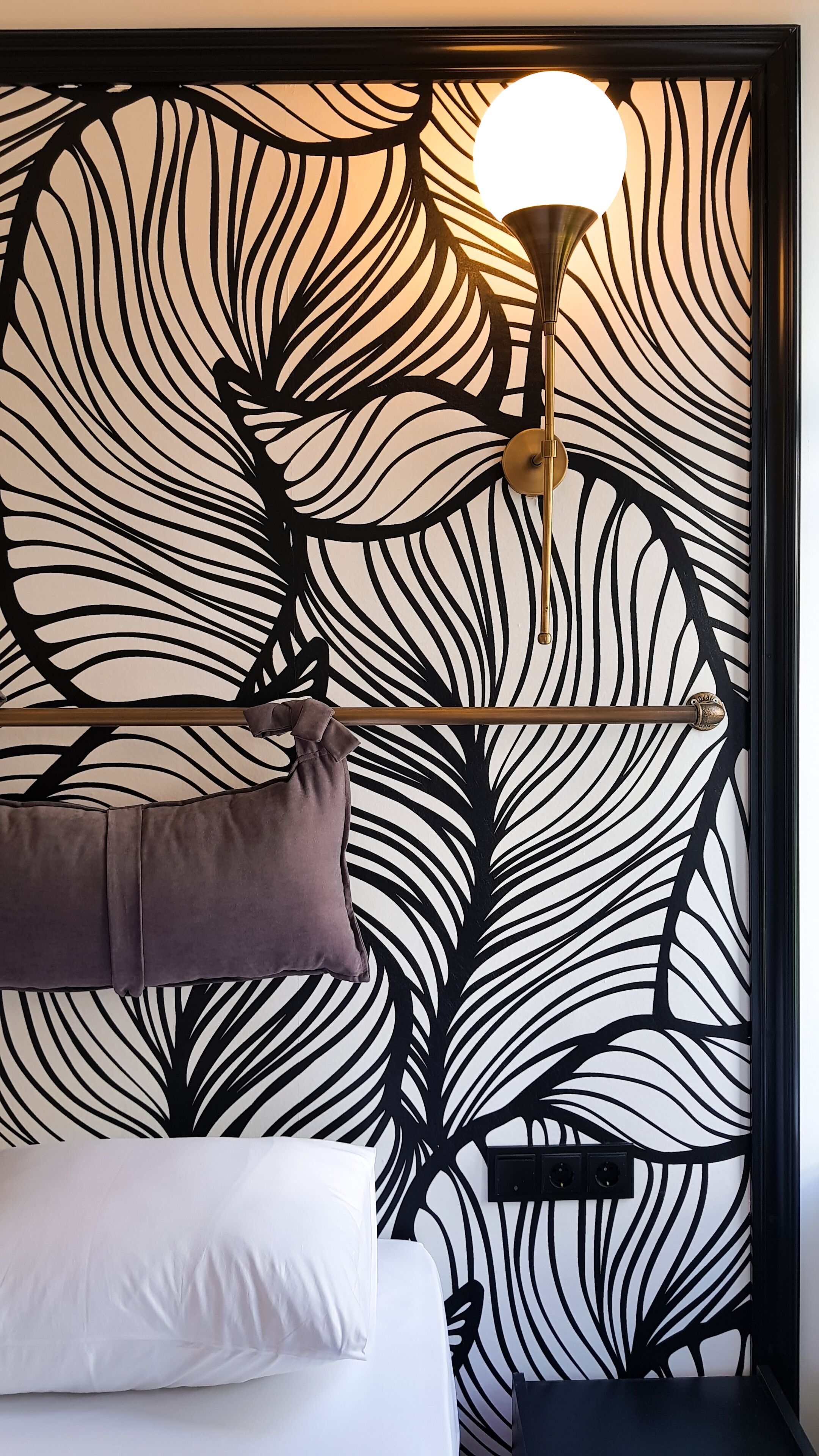 A bedroom with a bed, a nightstand, a lamp, and a wall with a leaf pattern.