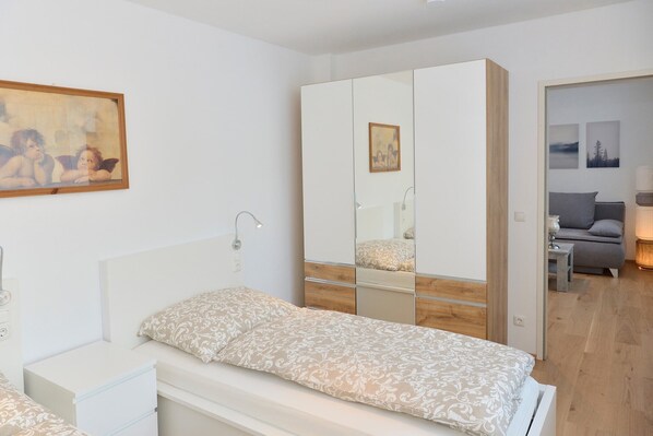 A bedroom with a bed, a wardrobe with mirrors, a bedside table, and a painting on the wall.