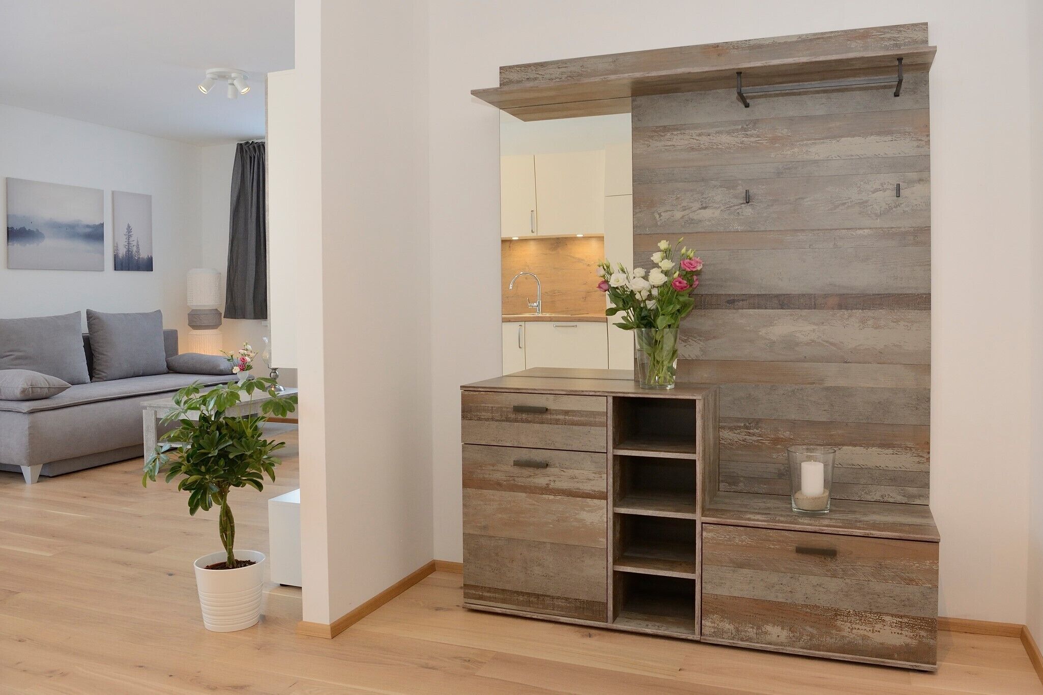 Una sala de estar moderna con un sofá gris, una mesa de centro blanca, una planta en maceta, un mueble de madera con cajones y un espejo.