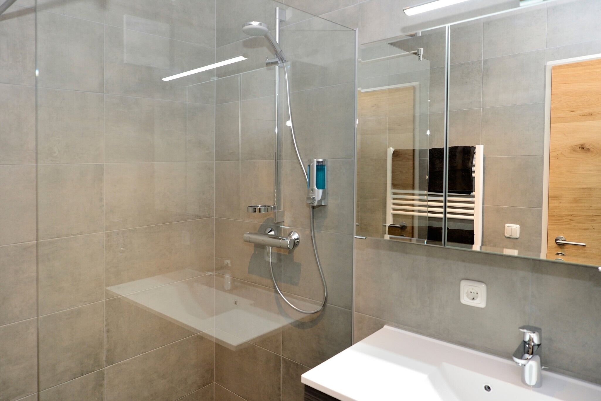 A modern bathroom with a glass shower enclosure, a white sink, and a mirror reflecting a wooden cabinet.