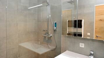 A modern bathroom with a glass shower enclosure, a white sink, and a mirror reflecting a wooden cabinet.