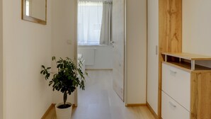 Ein Flur mit einem Topfpflanzen, einem Holzschrank und einer Tür zu einem Zimmer mit Fenster und Vorhängen.