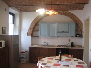 A kitchen with a brick arch, white cabinets, a refrigerator, and a table with a bottle.