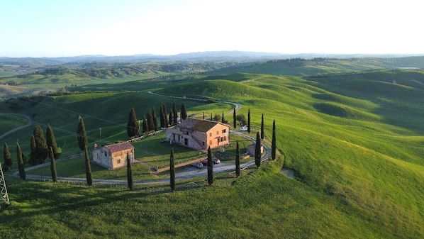 A rural landscape with rolling hills, a small stone house, and a few trees.