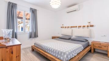 A bedroom with a wooden bed, a bedside table, a nightstand, a hanging light fixture, and a window with curtains.
