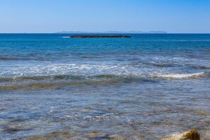 A coastal view with clear blue water, a rocky outcrop, and distant landforms.