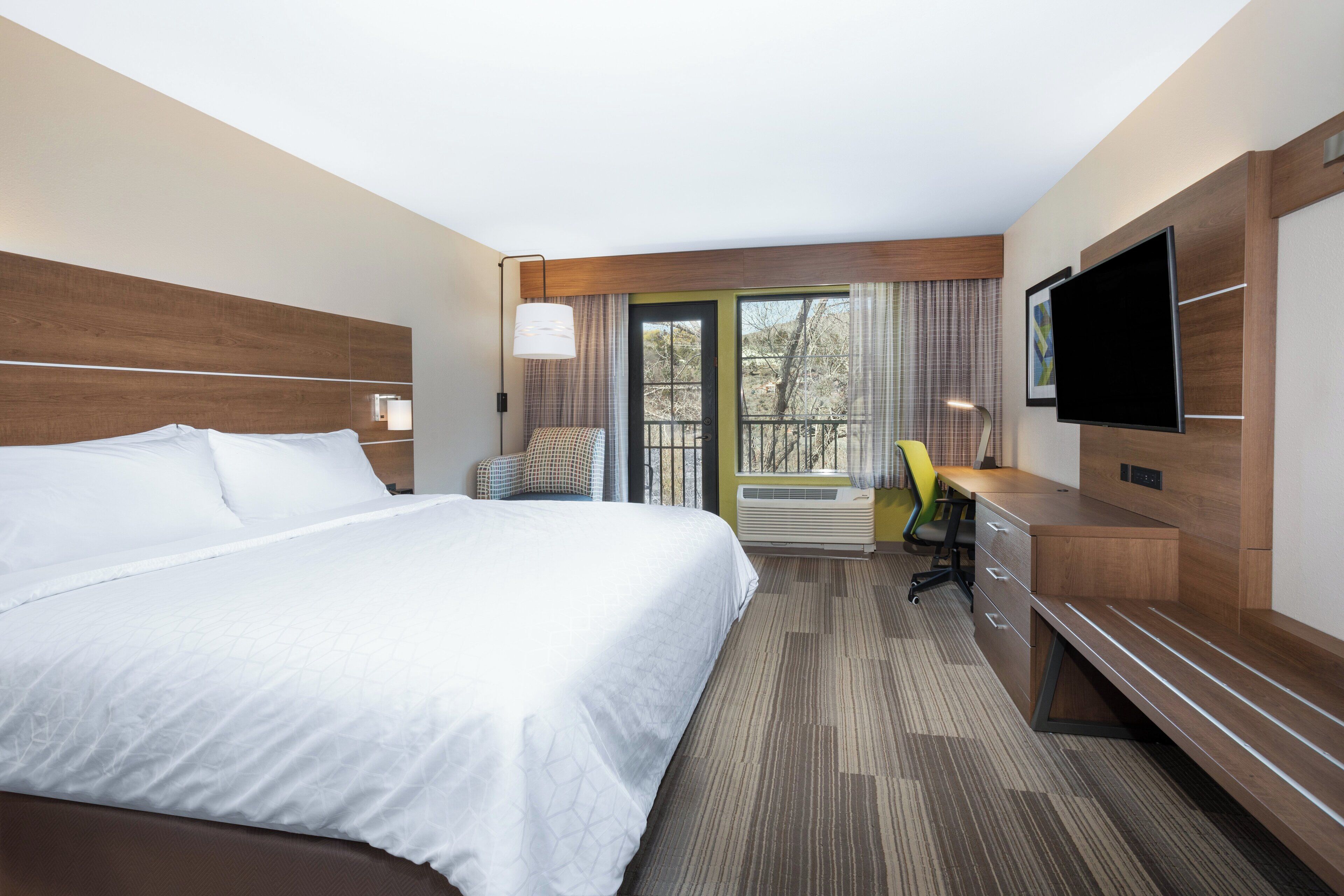 Een hotelkamer met een groot bed, een bureau met lades, een stoel, een televisie en een raam met gordijnen.