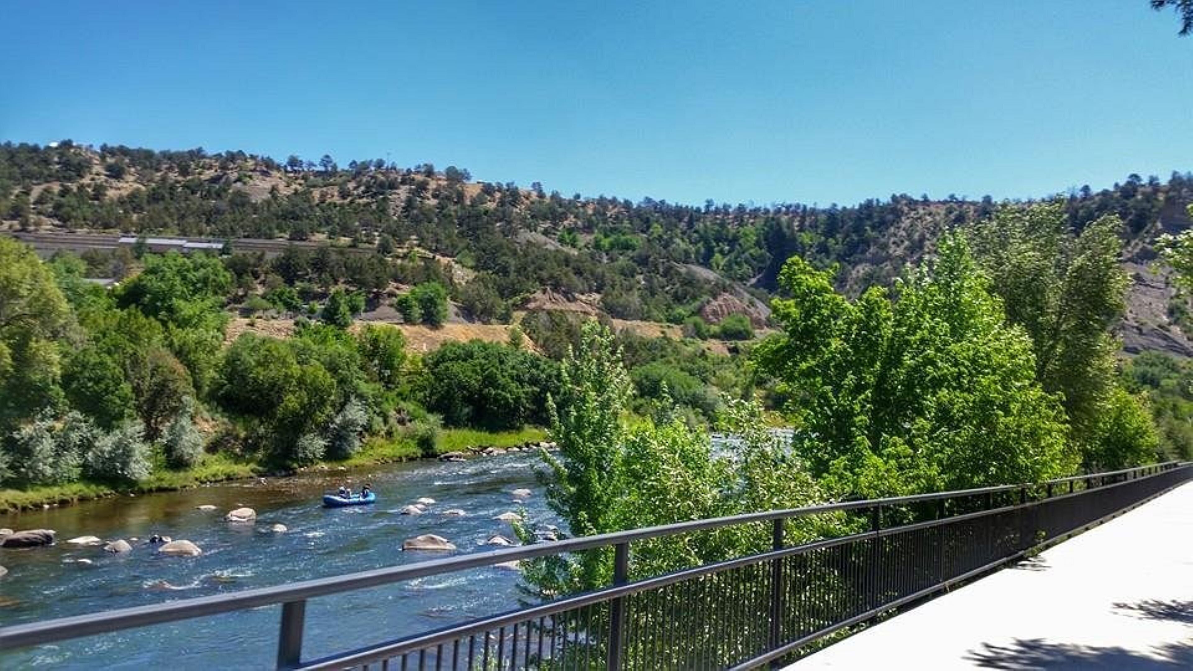 Un río con un puente y una ladera boscosa al fondo.