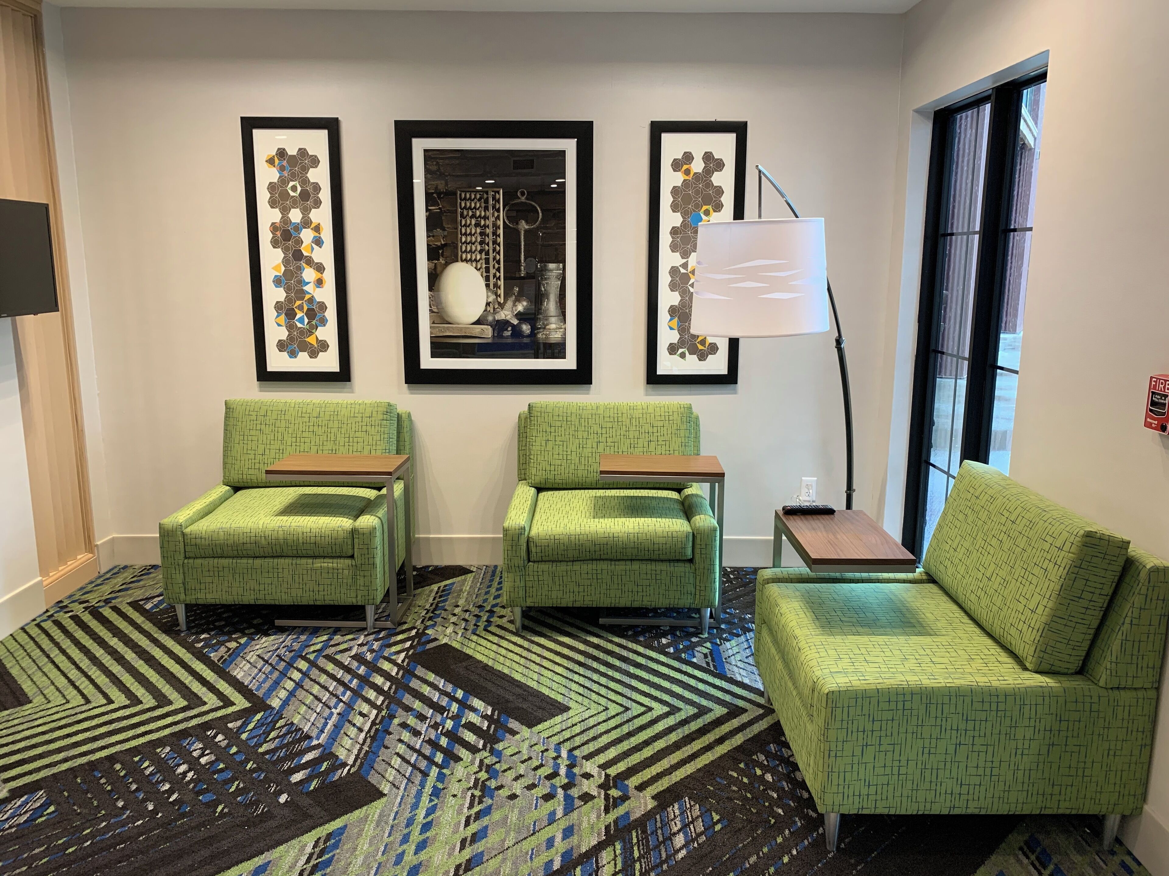 A room with two green armchairs, a sofa, a patterned rug, and three framed artworks on the wall.