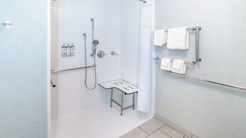 A modern bathroom with a glass shower enclosure, a handheld showerhead, a handheld showerhead, a glass-enclosed bench, and a towel rack with towels.