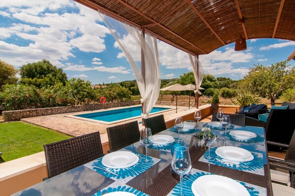 An outdoor dining area with a pool, covered seating, and a view of the landscape.
