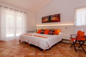A bedroom with a large bed, a painting on the wall, and a chair.
