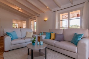 A spacious living room with two sofas, a coffee table, and a view of the outdoors through large windows.