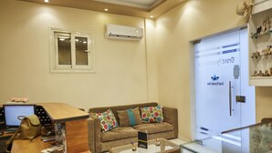 A reception area with a wooden desk, a brown sofa with colorful pillows, a glass coffee table, and an air conditioning unit on the wall. - Grand Pyramids View Guesthouse (Giza)