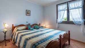 Ein Schlafzimmer mit Bett, Nachttischen, einem Fenster mit Vorhängen und einem Wandbild.