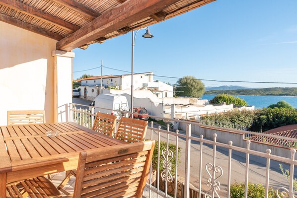 Un tavolo e sedie di legno su un balcone con vista su una cittadina costiera e montagne.
