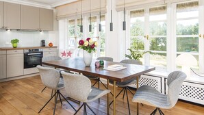 A spacious kitchen with modern appliances, a dining area with a wooden table and chairs, and large windows offering a view of the outdoors. - Wattenhof 3 from A&M - Wattenhof 3 (Kampen (Sylt))