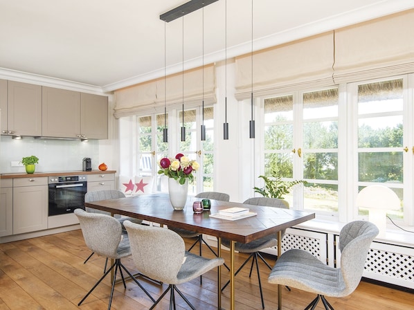 A spacious kitchen with modern appliances, a dining area with a wooden table and chairs, and large windows offering a view of the outdoors.