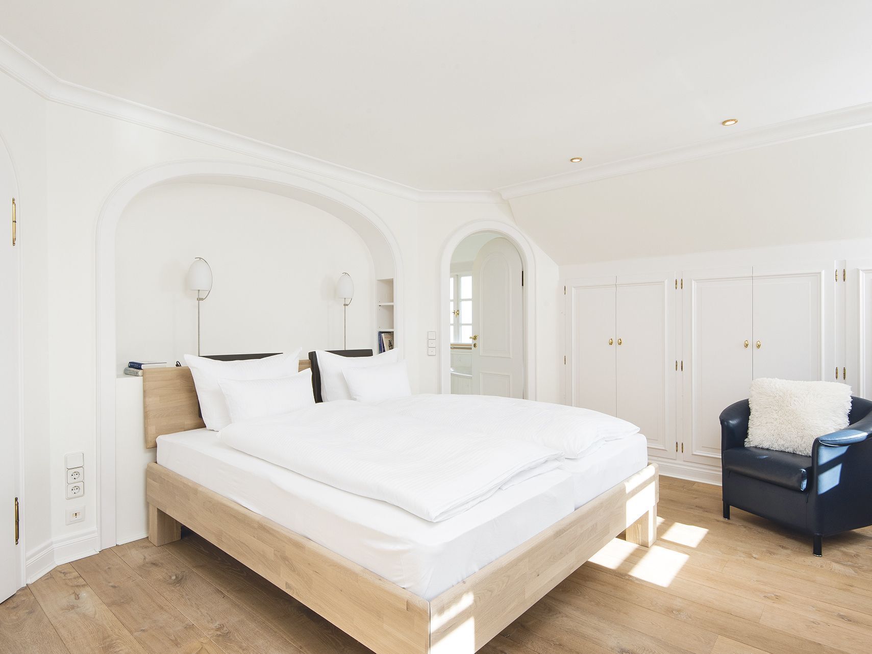 A spacious bedroom with a large bed, wooden headboard, and a black armchair.