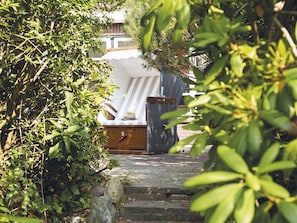 A covered outdoor seating area with a striped bench and a hat on it, surrounded by greenery.